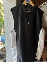 Black Nike Jordan sleeveless tank top with white side panels hanging on a wooden hanger, showing front view and white Jumpman logo on chest