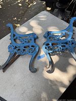 Pair of blue painted antique cast iron bench ends shown from a top perspective on a table, highlighting the overall shape and details of the metalwork.