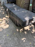 Side and top angled view of a large black plastic tool box for pickup truck bed showing textured surface and locking slot.