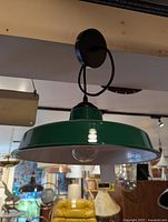 Green enamel pendant light fixture hanging from ceiling; wide green glossy shade with white interior visible, black hanging cord and fixture mount seen.
