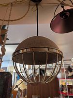 Photo of a modern pendant light featuring a cement dome shade with a silver metal cage around the bulb area, hanging from a black cord.