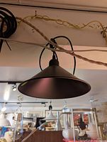 Black modern pendant light hanging from the ceiling with a conical shade and black cord, showing the item's shape, color, and hanging mechanism.