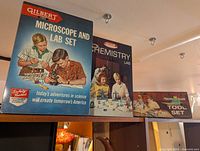 Photo showing three vintage metal educational kit boxes by Gilbert: Microscope and Lab Set, Chemistry Lab, and Tool Set.