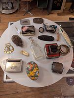 Wide view of all the items in the lot arranged on a white round table showing diverse vintage collectibles including a toy motorcycle and painted egg container.
