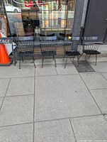 Four black wooden chairs with hairpin metal backs and legs arranged side by side outdoors.
