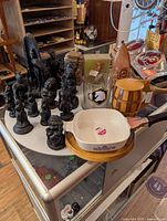 Photo showing multiple tiki and Polynesian-style figurines on glass cart with various kitchenware including CorningWare dish and wooden barrel container