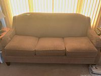Front view of tan three-seat upholstered sofa with three seat cushions and wooden legs