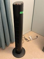 Full view of black tower fan standing on base with power cord visible