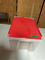 Full view of clear plastic storage bin with red split lid on table