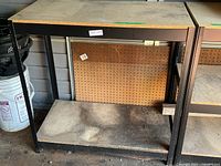 Full view of shelving unit showing metal frame, two particle-board shelves, pegboard panel