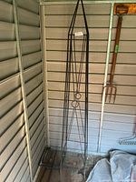 Full view of black metal obelisk trellis leaning in shed corner