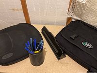 Group shot showing messenger bag, padded case, three-hole punch and pen holder with pens
