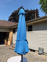 Full view of closed patio umbrella showing blue canopy and black pole