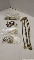 Various pearl necklaces in plastic bags, metal chain necklaces, and bracelet on white background.