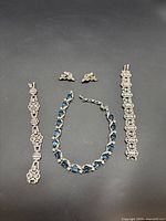 All four pieces laid flat on black background: necklace centered, bracelets at sides, earrings at top