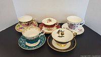 Set of 5 bone china cups and saucers with varied floral and decorative designs arranged on a table.