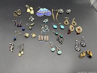 Wide view of all 22 pairs of mixed vintage clip-on and semi-precious stone earrings in various styles spread on a black surface
