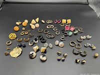 Multiple sets of earrings and singles arranged on a flat surface with various designs, colors, and materials seen clearly