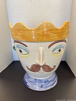 Front view of a large egg-shaped ceramic planter with a painted face of a man with a mustache and a yellow crown top.
