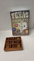 Wooden Tic Tac Toe game board with wooden X and O pieces in a 3x3 grid next to a boxed Texas Hold'em card game, which is new and unopened.