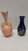 Both decorative porcelain vases shown together on white surface, pink Lenox vase with gold handles, and cobalt blue floral design vase.