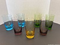 Seven Mid-Century Modern colored glass tumblers grouped together showing the variety of colors: blue, purple, yellow, and green.
