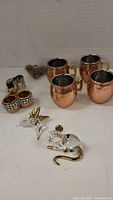 Miniature copper mugs and glass animal figurines tipped with gold color on white background.