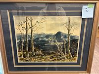 Framed watercolor landscape painting showing the full artwork with trees, mountains, and a water body.
