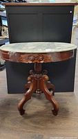 Full view of oval marble top end table with carved wood base showing overall structure and condition.