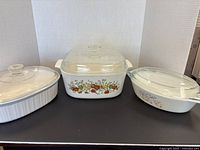 Front view showing three large casserole pots with glass lids arranged side by side on a black surface.