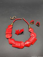 View of red wooden geometric bead necklace with three pairs of earrings: red star, red and black triangular, and gold-tone hoops.