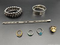 Full view of two stretch bracelets, one metal link bracelet, and four rings showing colors and style