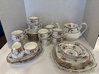 Full set arranged showing cups stacked on saucers at center, side plates and serving dishes at right, teapot at back right, milk jug and sugar bowl at front.