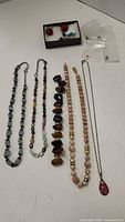 Seven stone necklaces and pair of red bead earrings in box, plus some loose stones in plastic bag on a white surface.