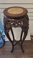 Full view of the vintage carved wood plant stand with stone insert on top, showing the floral carved details and curved legs.