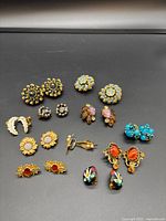 Photo of a variety of 12 pairs of vintage clip-on earrings including floral, rhinestone, enamel, and faux pearl designs in gold-tone and colorful finishes.