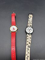 Two vintage Disney Mickey Mouse wristwatches, one with red leather strap and gold-tone case, the other with black case and patterned strap.