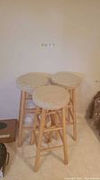 Photo showing three pine base bar stools with round beige corduroy style seats clustered together on tiled floor.
