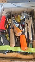 View of mixed hand tools including screwdrivers, pliers, and a vise grip inside a cardboard box