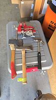 Four hand tools laid out on a folding table: red Sears bench vise, hatchet, mini splitting maul, and Stanley hammer