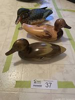 Three wooden duck figurines arranged on a tiled surface showing color and size variation for the lot.
