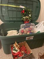 Large green Rubbermaid tote with open lid showing assorted Christmas decorations including baubles in smaller containers and various figurines inside and around the tote.