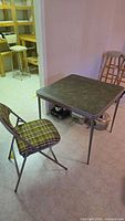 Card table with green marbled top and one folding chair with plaid fabric upholstery visible.