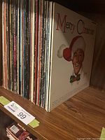 Shelf with a row of various vinyl LP records including a Merry Christmas album with a man in a Santa hat on the cover.