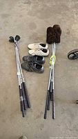 Photo of golf clubs grouped with two pairs of golf shoes on a concrete floor.