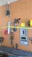 Variety of hand tools mounted on pegboard including caulking gun, various clamps, scissors, and shears near an electrical panel.