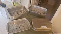 Set showing multiple stainless steel roasting pans and perforated trays arranged on a table.
