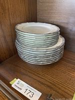 Stack of off-white bone china plates and bowls with scalloped edges showing the detailed pattern on rims.