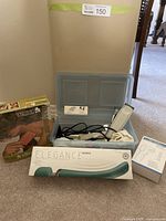 Photo showing two body/muscle massagers, a Wahl branded massager in original box, an Elegance branded massager device, infrared thermometer, and hair trimmer kit in a grey plastic container.