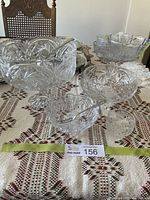 Set of clear pinwheel patterned crystal glass serving pieces arranged on a woven tablecloth with label number 156. Includes a pedestal compote with spoon, fruit bowl, pickle bowl with fork, and sugar bowl.
